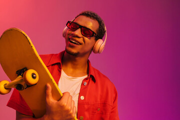 African guy posing with skateboard isolated over gradient neon background