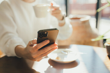 A woman using smartphone and drinking fragrant coffee in a cafe.