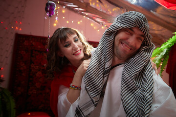 Portrait of young arabian muslim couple in traditional clothes in cozy red room. Fhoto shoot in easten style with male and female model like in a harem with a sultan and an odalisque. Partial focus