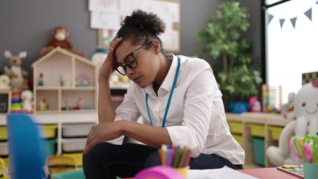 African american woman teacher sitting on chair stressed at kindergarten