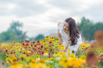 Fototapeta premium Beautiful Asian woman in garden with colorful flowers in foreground natural beauty while relaxing in the garden. Happy girl with flower field dress, travel concept.