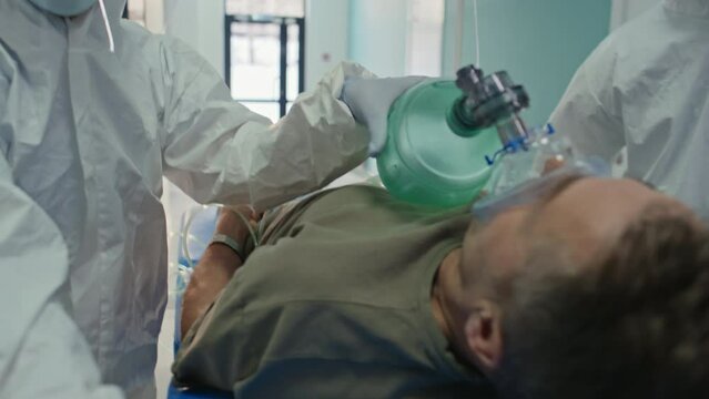 Tracking shot of unrecognizable paramedic service workers performing artificial ventilation to patient using bag valve mask while bringing him to intensive care unit