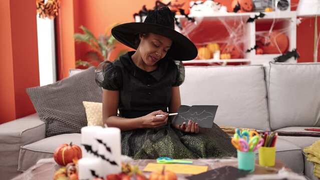 African american woman wearing witch costume drawing bat decoration at home