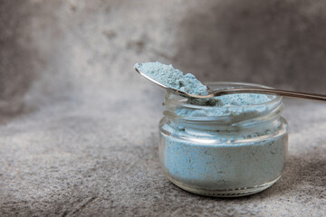 Blue spirulina powder in a bowl on a black textured surface. Natural vegan superfood. Healthy food supplement. Phycocyanin extract. Place for text. Place for a copy.