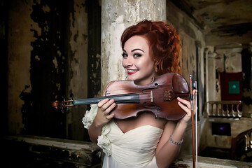 Pretty young cover woman holding violin at medieval castle interior background, looking at camera....