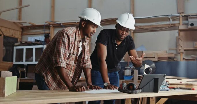  two African males discussing blue print in carpentry factory 