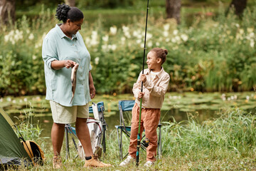 Full length portrait of happy mother and daughter fishing together during camping in nature