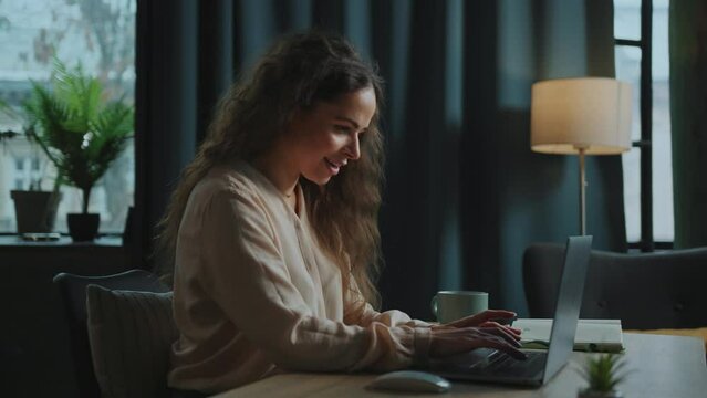 Footage of happy good-looking young Caucasian woman chatting in messenger on Internet and using laptop. Portrait of pleasant-looking girl typing on keyboard, reading messages in loft office