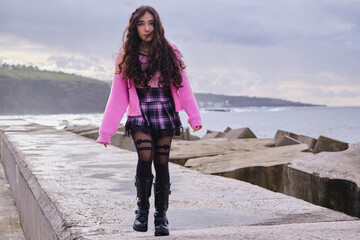Teenage girl wearing gothic pastel style in black and pink colours laughs while posing by the sea.