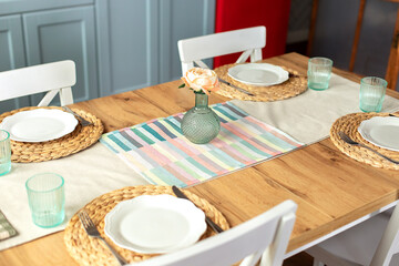Table setting for dinner at home. Beautiful served table with runner on table, vase with flowers and plates in living room. Stylish dining room with table and wooden chairs. Cozy kitchen with dishes.	