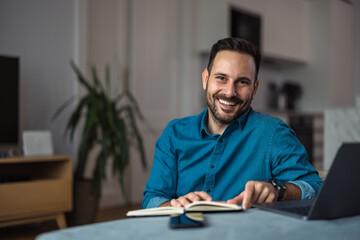Portrait of a busy man, working over the laptop and holding a notebook, indoors.