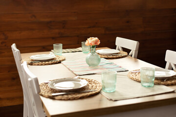 Table setting for dinner at home. Beautiful served table with runner on table, vase with flowers and plates in living room. Stylish dining room with table and wooden chairs. Cozy kitchen with dishes.	