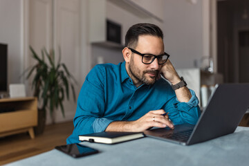 Focused male employer surfing the web over the laptop, sitting on the home floor.