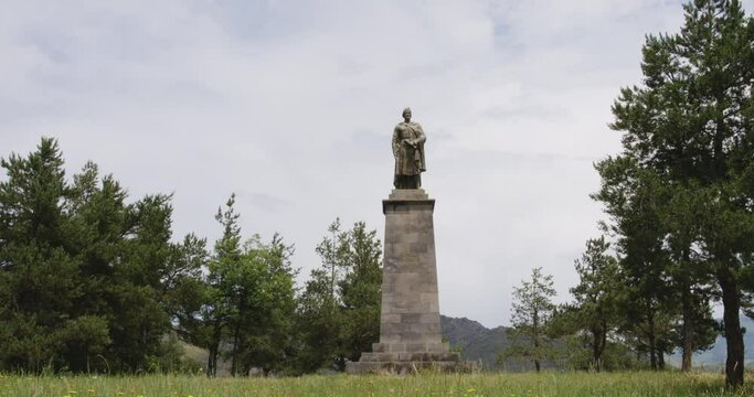 Statue of Shota Rustaveli on stone pedestal in georgian countryside.