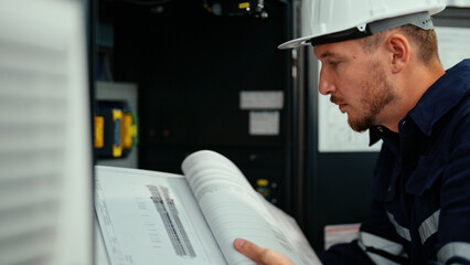 Fototapeta na wymiar Caucasian production engineer in safety wear is reading the manual of a machine to find an error. A male factory worker is checking the industrial control panel of a robotic machine for maintenance.