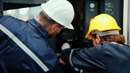 Back view of two Caucasian production engineers in safety wear assisting in adjusting and maintaining CNC machine in the factory. Male factory workers are examining the industrial machine to fix it.