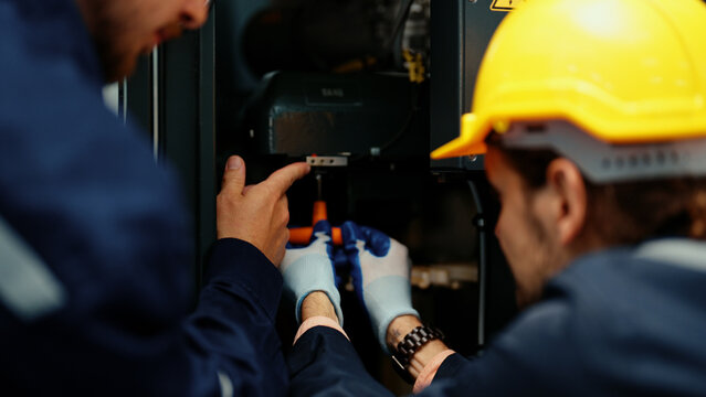 Close-up of two&nbsp;Caucasian production engineers in safety wear assisting in adjusting and maintaining CNC machine in the factory. Male factory workers are examining the industrial machine to fix it.