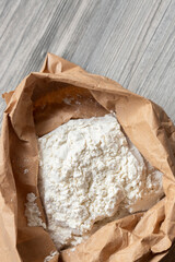 Plain white flour in a brown paper bag on grey wood. Eco friendly biodegradable recycle packaging