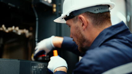 Close-up of Caucasian production engineer in safety wear inspecting CNC machine to fix an error. A...