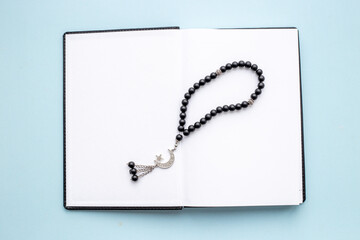 Fototapeta na wymiar Koran book and black Muslim rosary with silver crescent moon