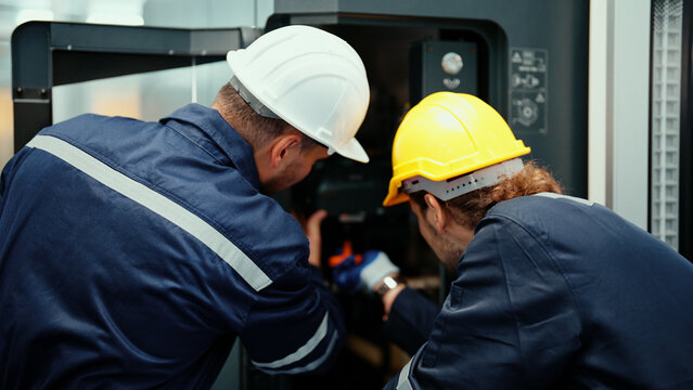 Back view of two&nbsp;Caucasian production engineers in safety wear assisting in adjusting and maintaining CNC machine in the factory. Male factory workers are examining the industrial machine to fix it.