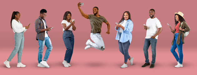 Happy millennial black people in casual chatting on smartphone, taking selfie, jump, on pink...