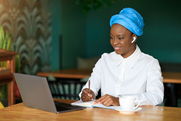 Positive young black woman attending online business meeting, cafe interior