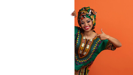 Cheerful african woman in traditional costume pointing at advertising board