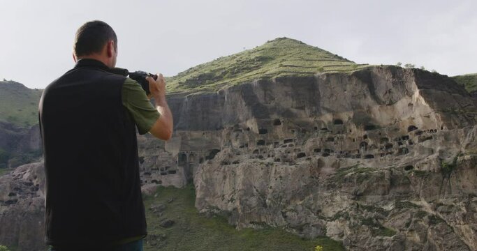 Man with professional camera taking photos of Vardzia cave monastery.
