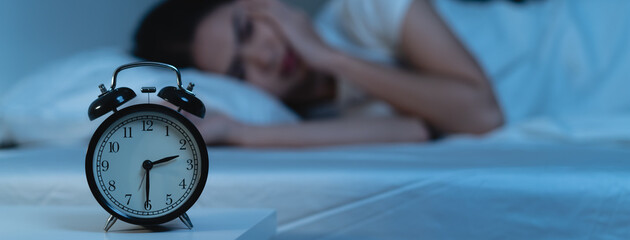 Close-up alarm clock on the table have a sleepless woman as background