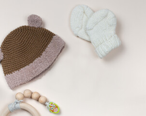 Beige background with a knitted hat, booties and a wooden rattle. Eco-friendly products for...