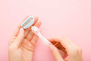 Young adult woman hands holding razor and changing new head on light pink table background. Pastel...