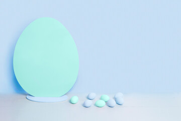 Big blank turquoise Easter egg and small blue and turquoise easter eggs on the background of blank blue wall. Minimalist Easter background