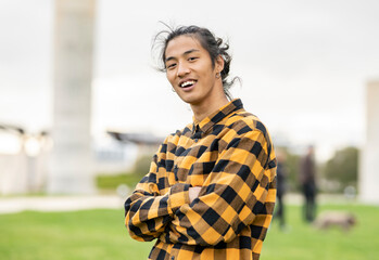 portrait of handsome asian man with long hair, outdoors in casual clothes, arms crossed looking at camera