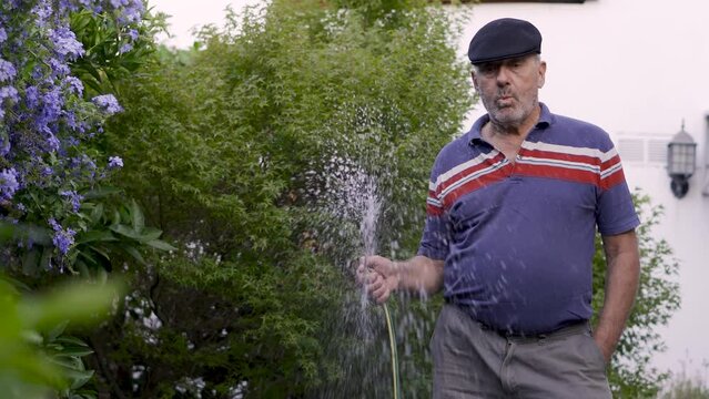 Retired old man waters his garden while whistles a song.