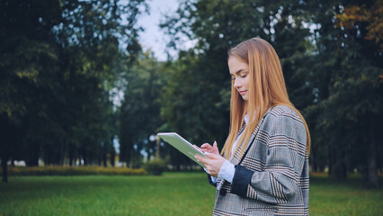 A young girl walks with a tablet in the park.