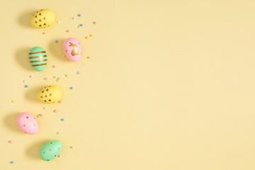 Fototapeta na wymiar Easter holiday composition. Easter eggs colorful confetti sugar candy sprinkles on isolated pastel yellow background. Easter concept. Flat lay, top view, copy space 
