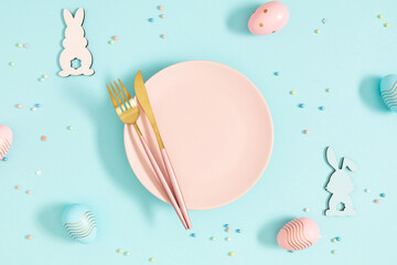 Easter holiday composition.Top view of pink plate with easter eggs with knife and fork and wooden...