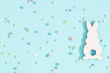 Easter holiday composition. Easter wooden bunny toy, colorful sugar candy sprinkles on isolated pastel blue background. Easter concept. Flat lay, top view, copy space 