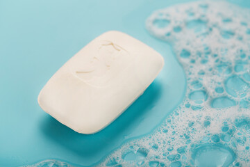 A piece of white soap with foam on blue background. Backdrop with copt space.