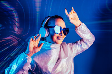 Portrait of a smiling dancing woman in sunglasses and headphones in neon light. Music lover. Silent...