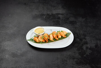 Appetizer of deep-fried shrimps with sauce. Crispy shrimps in tempura on black background. Fried prawns in asian style on dark concrete table. Asian prawns with sauce in minimal style.