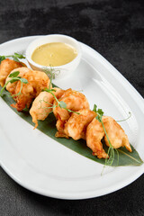 Appetizer of deep-fried shrimps with sauce. Crispy shrimps in tempura on black background. Fried prawns in asian style on dark concrete table. Asian prawns with sauce in minimal style.