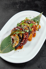 Delicatessen appetizer - grilled octopus with eggplant in teriyaki sauce. Boiled octopus tentacle and vegetables in pan asian style. Salad with octopus and eggplant in miso sauce on black table.