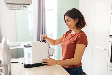 Fototapeta na wymiar Smiling Young Arab Woman Preparing Coffee With Machine In Kitchen