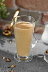 Masala tea on transparent cup. Indian tea with milk and spices on concrete background. Black tea with milk and on upright glass on stone backdrop