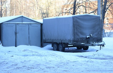 A large gray four-wheeled trailer stands near a metal garage