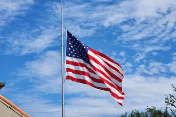 USA national flag waving lowered to half mast on wind against blue sky. American stars and stripes...