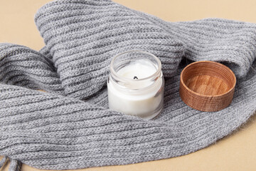 Handmade candle in a glass with wooden lid on grey scarf