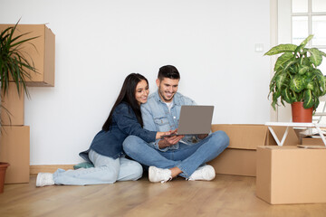Moving Concept. Smiling Couple Using Laptop While Sitting On Floor In Apartment